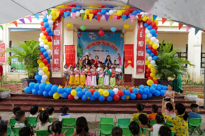 A group of children on stage with balloons and a group of kidsDescription automatically generated