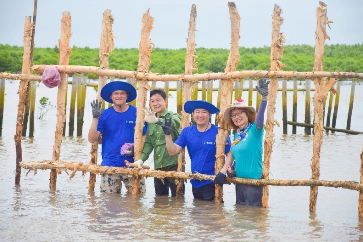 A group of people standing in water holding a wooden frame

Description automatically generated