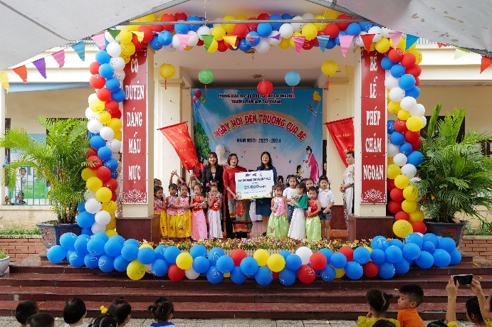 A group of children standing in front of a building with balloons

Description automatically generated
