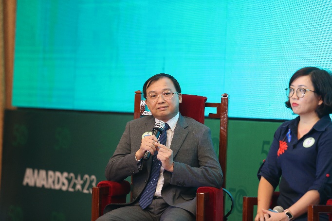 A person in a suit sitting in a chair with a microphoneDescription automatically generated