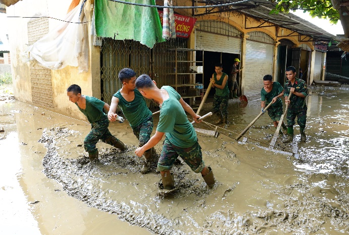 A group of people in green shirts digging in mud

Description automatically generated