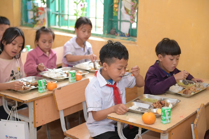 A group of children eating at a schoolDescription automatically generated
