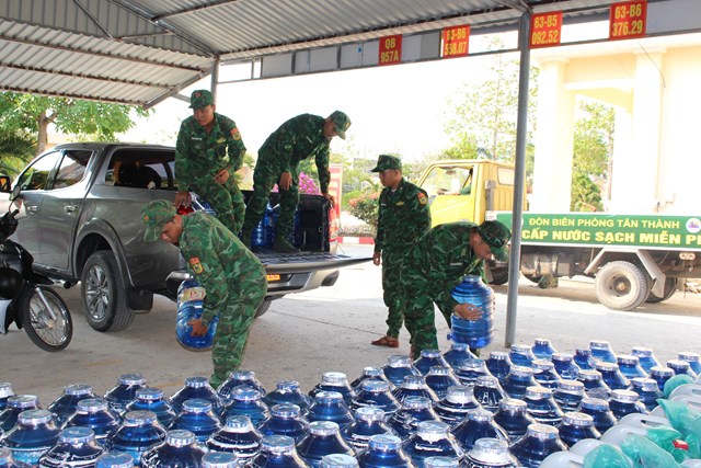 Cán bộ, chiến sĩ Đồn Biên phòng Tân Thành vận chuyển từng bình nước uống lên xe ô tô bán tải để đưa đến các điểm, các hộ gia đình cấp phát cho người dân.  