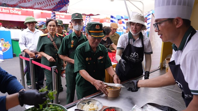 Cựu chiến binh nữ trong màu áo xanh quân đội vui vẻ nhận phần bánh đa cua nóng hổi tại gian hàng Hải Phòng.