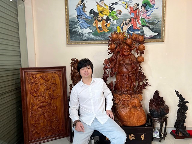 Nghệ nh&acirc;n Chu Đức Dũng (Dũng t&oacute;c) b&ecirc;n c&aacute;c t&aacute;c phẩm đi&ecirc;u khắc gỗ mỹ nghệ v&agrave; tượng thờ do ch&iacute;nh tay anh thực hiện, thể hiện kh&ocirc;ng gian s&aacute;ng tạo đậm dấu ấn thủ c&ocirc;ng truyền thống.